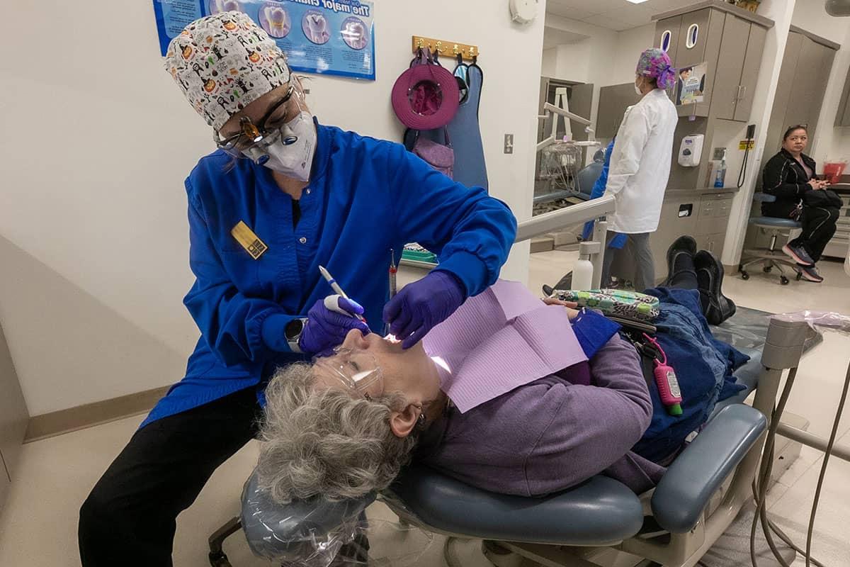一名学生卫生员正在检查一位躺在牙科椅上的妇女的口腔